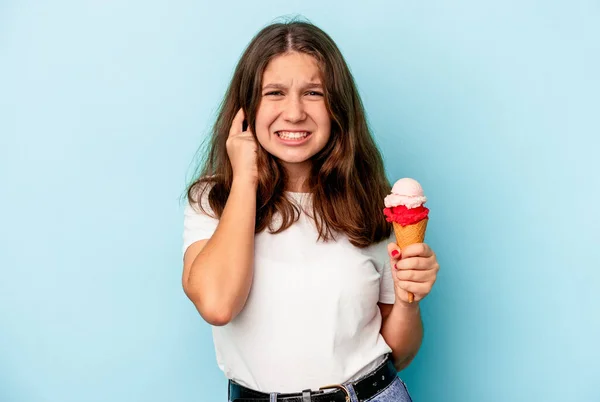一个白人小女孩正在吃一种用蓝色背景隔离的冰淇淋 用手捂住耳朵 — 图库照片