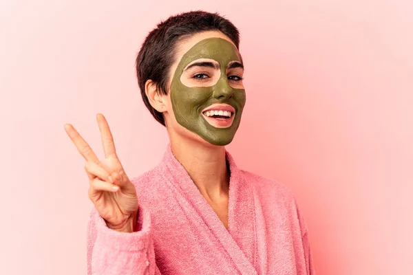 年轻的高加索女人戴着面具 与粉色背景隔离 快乐而无忧无虑 用手指展示和平的象征 — 图库照片