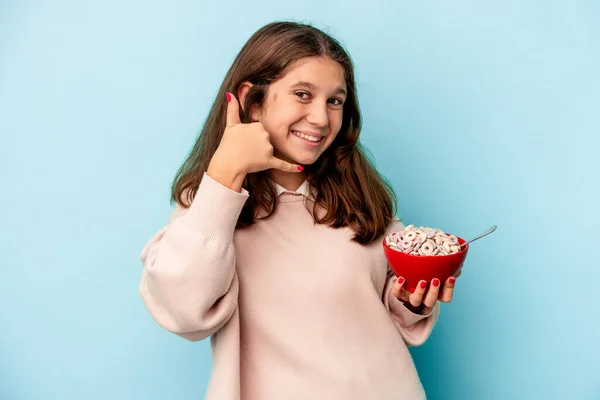 卡西亚小女孩拿着一碗谷物 蓝色背景隔离 用手指做一个手机通话手势 — 图库照片