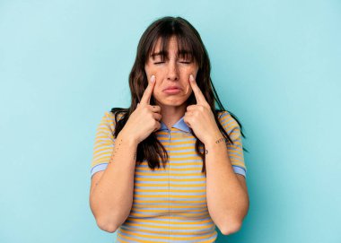 Arjantinli genç bir kadın mavi arka planda izole edilmiş, ağlıyor, bir şeyden memnun değil, acı ve kafa karışıklığı konsepti..