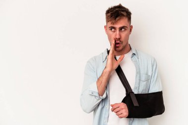 Beyaz arka planda izole edilmiş beyaz eli kırık genç beyaz bir adam gizli bir sıcak fren haberi veriyor ve yana bakıyor.