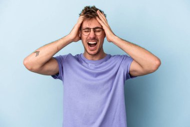 Genç beyaz adam mavi arka planda izole edilmiş bağırıyor, çok heyecanlı, tutkulu, bir şeyden memnun..