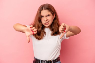 Pembe arka planda izole edilmiş küçük beyaz kız baş parmağını aşağı gösteriyor ve hoşlanmadığını ifade ediyor..