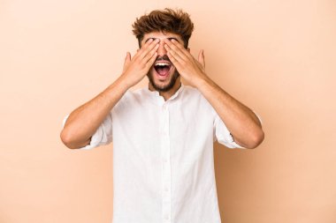 Bej arka planda izole edilmiş genç bir Arap. Gözleri ellerle kaplıyor. Gülümsüyor ve bir sürpriz bekliyor..