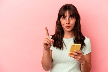 Elinde cep telefonu olan genç Arjantinli bir kadın pembe arka planda bir numarayı parmağıyla gösteriyor..