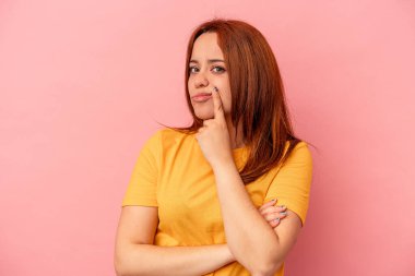 Pembe arka planda izole edilmiş genç beyaz kadın alaycı bir ifadeyle kameraya bakıyor..