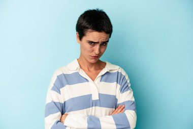 Mavi arka planda izole edilmiş genç beyaz kadın alaycı bir ifadeyle kameraya bakarken mutsuz oluyor..
