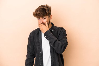 Genç Arap adam bej arka planda izole edilmiş. Ağzı elleri endişeli görünüyor..
