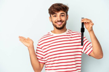 Mavi arka planda izole edilmiş bir kol saati tutan melez genç bir adam bir avuç içinde fotokopi alanı ve belinde başka bir el tutuyor..