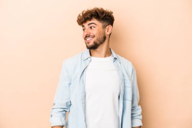 Genç Arap adam bej arka planda izole edilmiş gevşemiş ve mutlu bir şekilde gülüyor, boynunu uzatmış dişlerini gösteriyor..