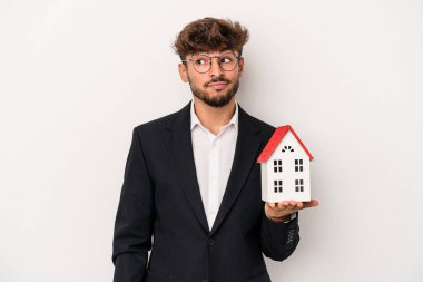 Genç Arap emlakçı, izole edilmiş arka planda bir model evi tutuyor. Kafası karışmış, şüpheli ve güvensiz hissediyor..