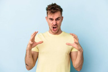 Mavi arka planda izole edilmiş genç beyaz adam öfkeyle bağırıyor..