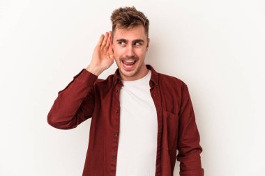 Beyaz arka planda izole edilmiş genç beyaz adam bir dedikoduyu dinlemeye çalışıyor..