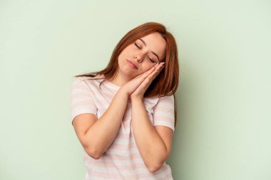 Yeşil arka planda izole edilmiş genç beyaz kadın esniyor. Ağzı eliyle kapatan yorgun bir jest gösteriyor..