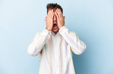 Mavi arka planda izole edilmiş genç beyaz adam yüzünün yarısını palmiye ile kaplayarak eğleniyor..