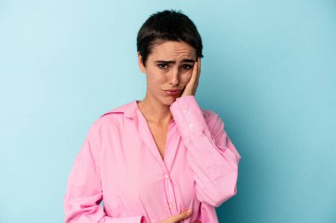 Mavi arka planda izole edilmiş genç beyaz kadın yanakları patlatıyor, yorgun bir ifadesi var. Yüz ifadesi kavramı.