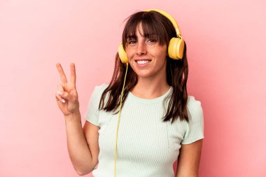 Pembe arka planda müzik dinleyen genç Arjantinli kadın iki numarayı parmaklarıyla gösteriyor..