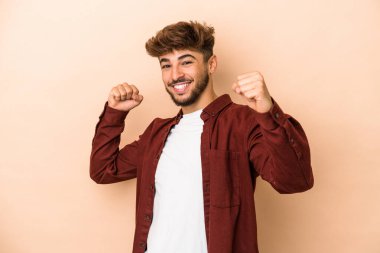 Genç Arap adam bej arka planda izole edilmiş tasasız ve heyecanlı tezahüratlar yapıyor. Zafer konsepti.