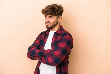 Genç Arap adam bej arka planda izole edilmiş şüpheli, belirsiz, seni muayene ediyor..