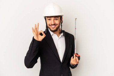 Miğfer takan ve taksimetre tutan genç mimar gri arka planda izole edilmiş neşeli ve kendinden emin..