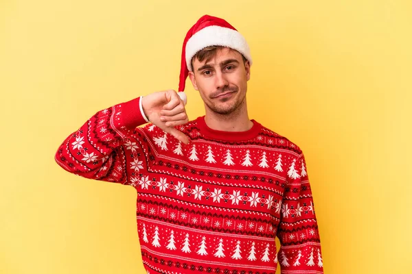 黄色の背景に隔離されたクリスマスを祝う若い白人男性は嫌なジェスチャー 親指を下に示しています 意見の相違 — ストック写真