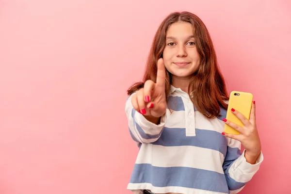 ピンクの背景に孤立した携帯電話を持っている小さなCaucasian女の子ショー数1とともに指 — ストック写真