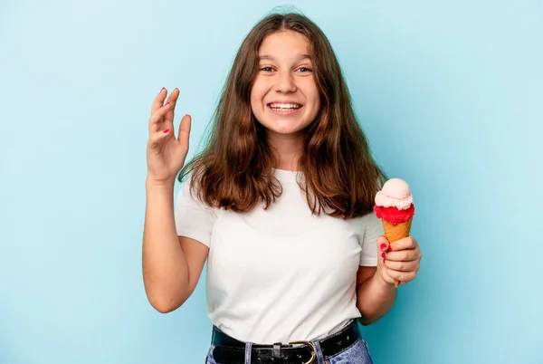 小高加索女孩吃着一个蓝色背景的冰淇淋 得到了一个愉快的惊喜 兴奋地举起了手 — 图库照片