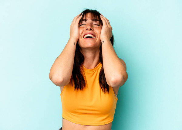 Young Argentinian woman isolated on blue background laughs joyfully keeping hands on head. Happiness concept.