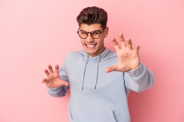 Pembe arka planda izole edilmiş genç beyaz adam pençelerini kedi taklidi yaparken gösteriyor, agresif bir hareket..