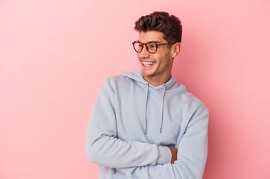 Pembe arka planda izole edilmiş genç beyaz adam kollarını kavuşturarak gülümsüyor..
