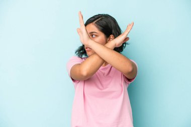 Mavi arka planda izole edilmiş genç Latin kadın iki kolu çapraz tutuyor, inkar kavramı.