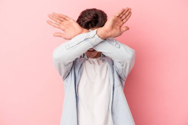 Pembe arka planda izole genç beyaz adam iki kolu çapraz tutuyor, inkar kavramı.