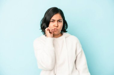 Mavi arka planda izole edilmiş genç Latin bir kadın parmakları dudaklarında bir sır saklıyor..