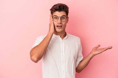 Pembe arka planda izole edilmiş genç beyaz adam, avuç içi fotokopi alanını elinde tutmaktan etkilenmiş..