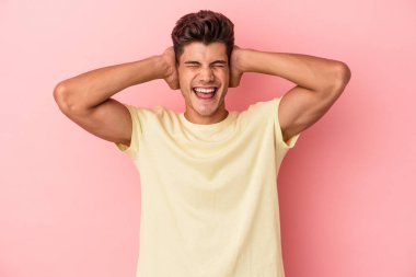 Kafkasyalı genç adam pembe arka planda izole edilmiş kulakları kulaklarıyla kapatıyor çok fazla ses duymamaya çalışıyor..