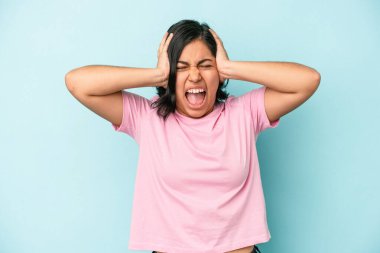 Genç Latin bir kadın mavi arka planda izole edilmiş kulakları kulaklarıyla kapatıyor çok fazla ses duymamaya çalışıyor..