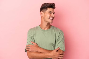 Pembe arka planda izole edilmiş genç beyaz adam kollarını kavuşturarak gülümsüyor..