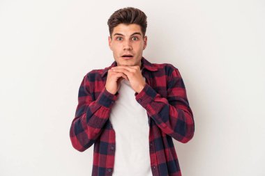 Beyaz arka planda izole edilmiş genç beyaz bir adam şans için dua ediyor, şaşırmış ve ağzını açıp önüne bakıyor..