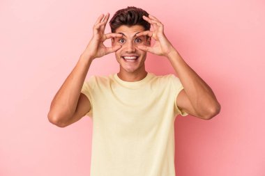 Pembe arka planda izole edilmiş genç beyaz adam bir başarı fırsatı bulmak için gözlerini açık tutuyor..