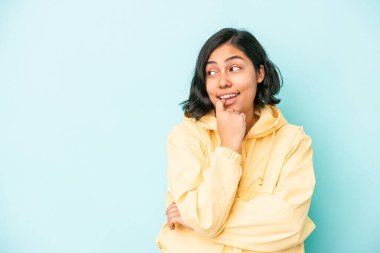 Mavi arka planda izole edilmiş genç Latin bir kadın rahatlamış bir şeyin fotokopi odasına baktığını düşünüyor..