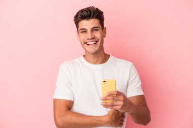 Pembe arka planda cep telefonu tutan genç beyaz adam gülüyor ve eğleniyor..