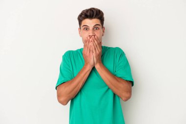 Beyaz arka planda izole edilmiş genç beyaz adam elleriyle ağzını kapatırken şok oldu..