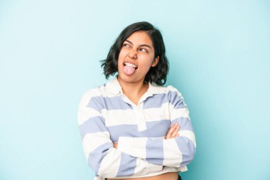 Mavi arka planda izole edilmiş genç Latin bir kadın. Komik ve dost canlısı bir dil uzatıyor..