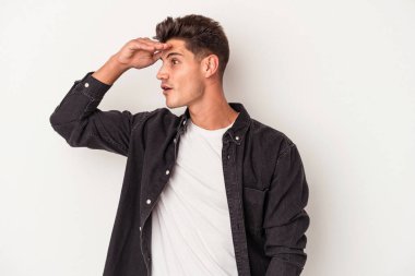 Beyaz arka planda izole edilmiş genç beyaz bir adam uzaklara bakıyor ve elini alnına koyuyor..