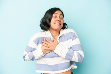 Mavi arka planda izole edilmiş genç Latin kadın, avuçlarını göğsüne bastıran dostça bir ifadeye sahiptir. Aşk konsepti.