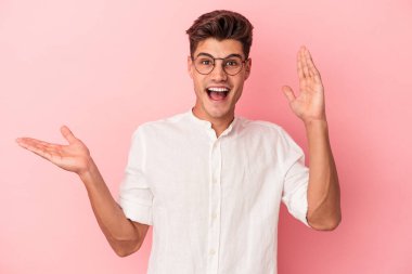 Pembe arka planda izole edilmiş genç beyaz bir adam avucunun içinde fotokopi alanı tutuyor, el üstünde tutuyor. Şaşırmış ve mutlu..