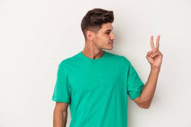 Beyaz arka planda izole edilmiş genç beyaz bir adam neşeli ve kaygısız parmakları olan bir barış sembolü gösteriyor..