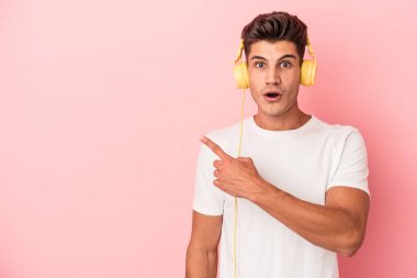 Pembe arka planda izole edilmiş müzik dinleyen beyaz bir adam yan tarafı işaret ediyor.