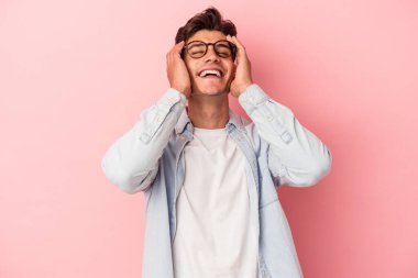 Pembe arka planda izole edilmiş genç beyaz adam ellerini başının üstünde tutarak neşeyle gülüyor. Mutluluk kavramı.