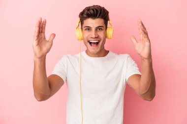 Pembe arka planda müzik dinleyen beyaz bir adam hoş bir sürpriz alıyor, heyecanlı ve el kaldırıyor..
